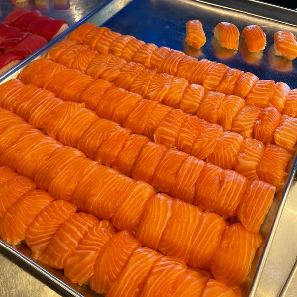 Rows of fresh salmon nigiri and tuna nigiri displayed on metal trays.