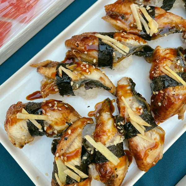 Unagi sushi with sweet sauce, sesame seeds, and ginger on a white rectangular plate.