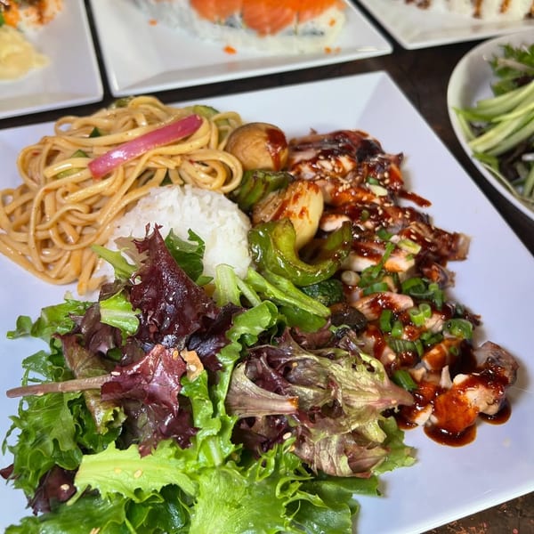 A white plate with teriyaki chicken, rice, noodles, salad, and vegetables.