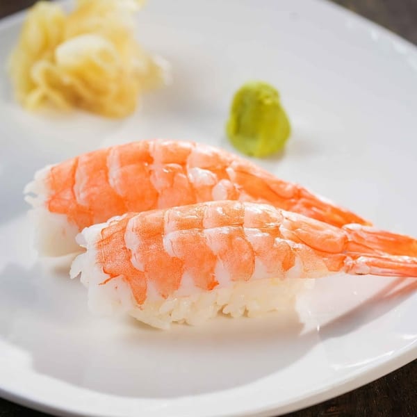 Two pieces of shrimp nigiri sushi with pickled ginger and wasabi on a white plate.